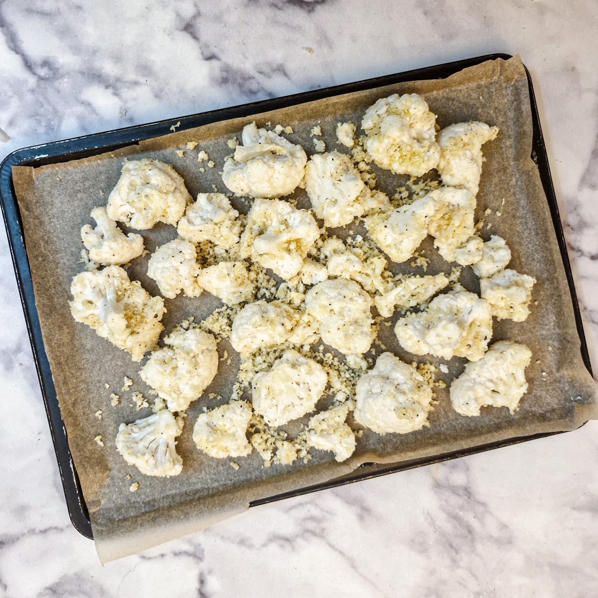 Raw pieces of cauliflower on a baking tray, coated with parmesan, olive oil and breadcrumbs.