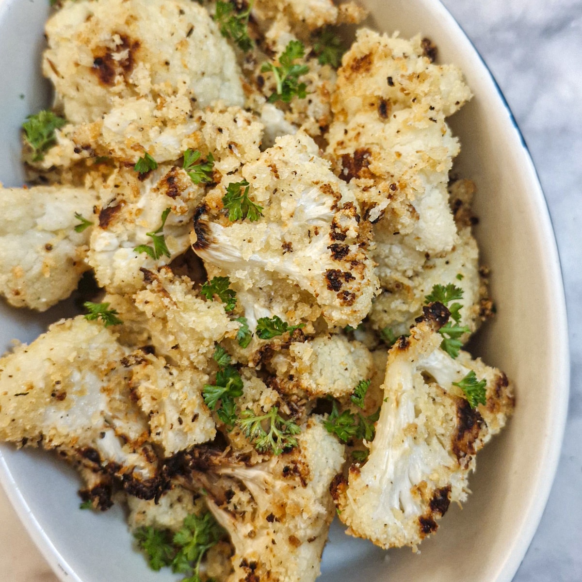 Roasted parmesan cauliflower in a serving dish, garnished with chopped parsley.