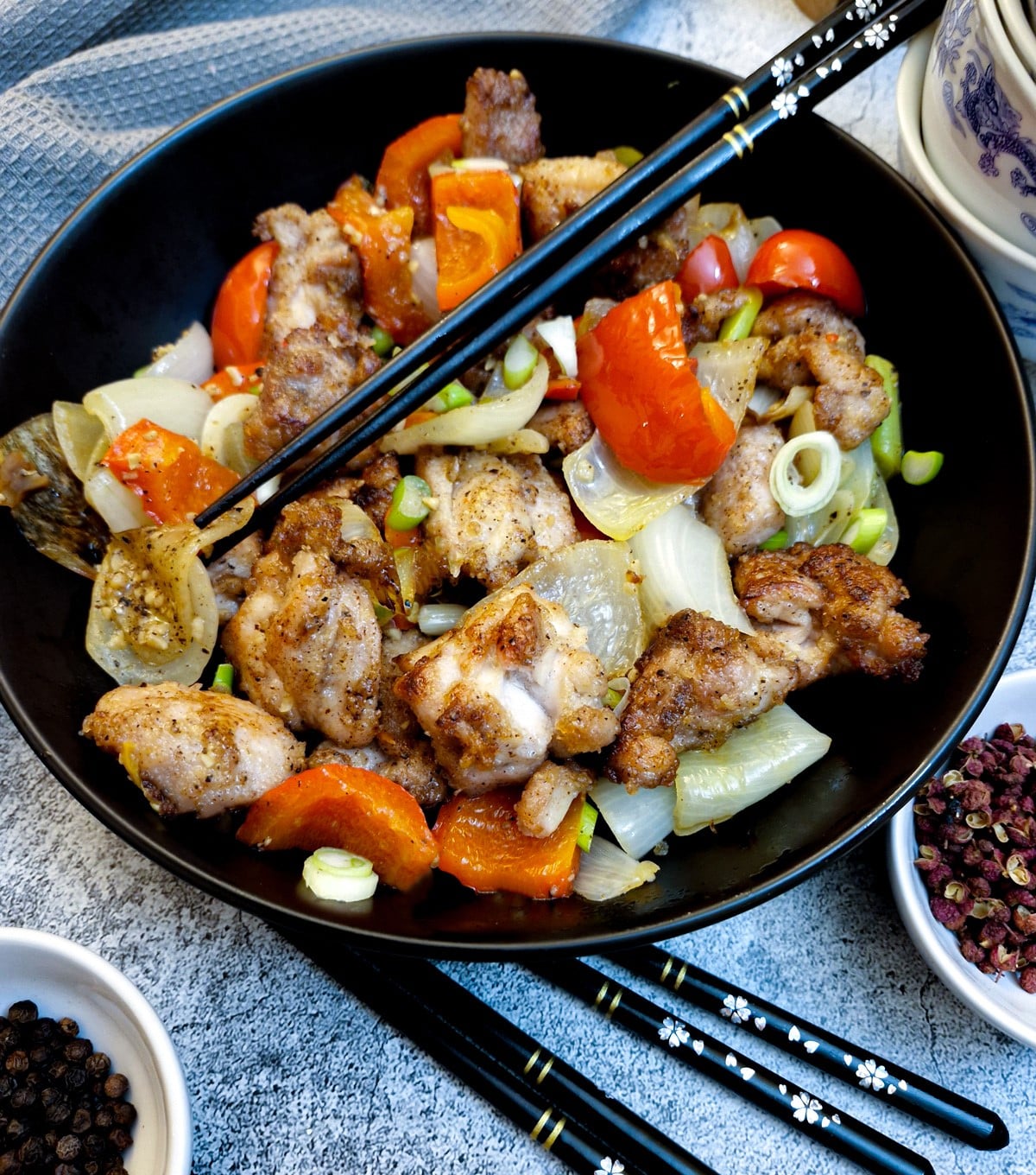 A black serving dish containing salt and pepper chicken.  There are black chopsticks in the dish.