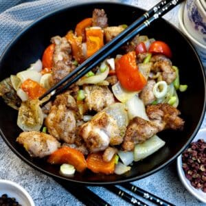 A black serving dish containing salt and pepper chicken. There are black chopsticks in the dish.