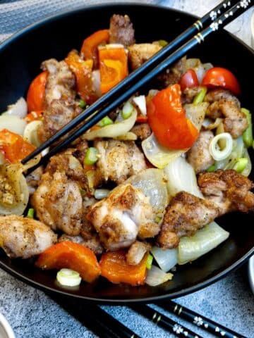 A black serving dish containing salt and pepper chicken. There are black chopsticks in the dish.