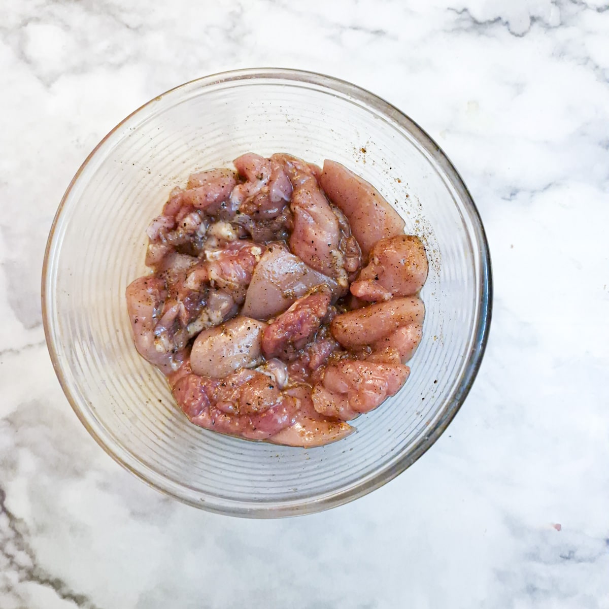 A glass dish with chicken pieces mixed into a marinade.