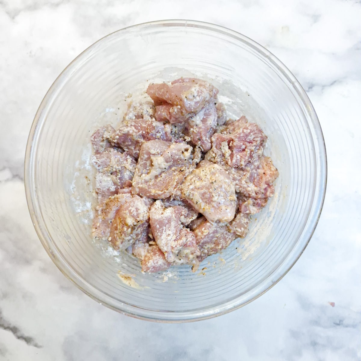 A glass bowl with pieces of marinated chicken coated in cornflour.