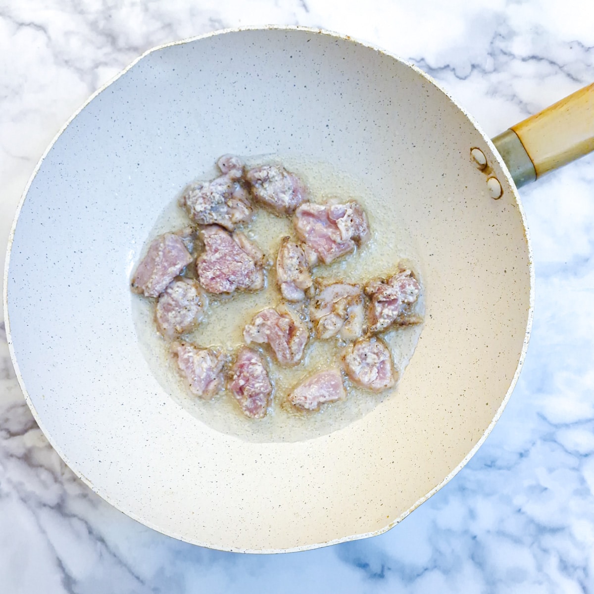 Chicken pieces frying in a wok.