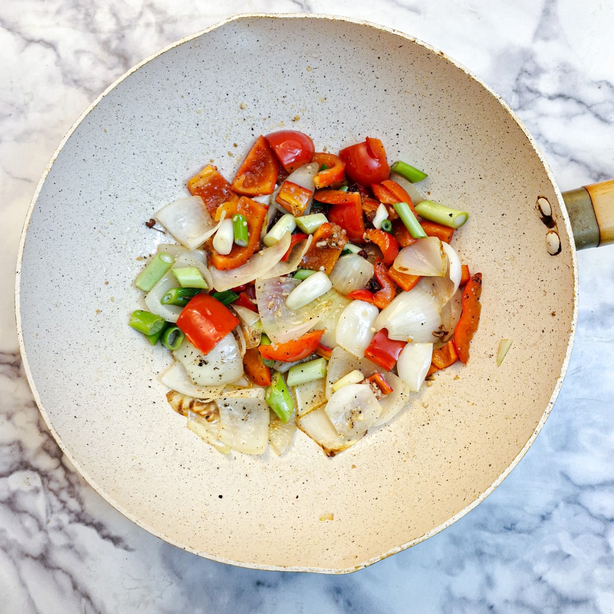 Onions and red peppers with chopped green spring onions frying in a wok.