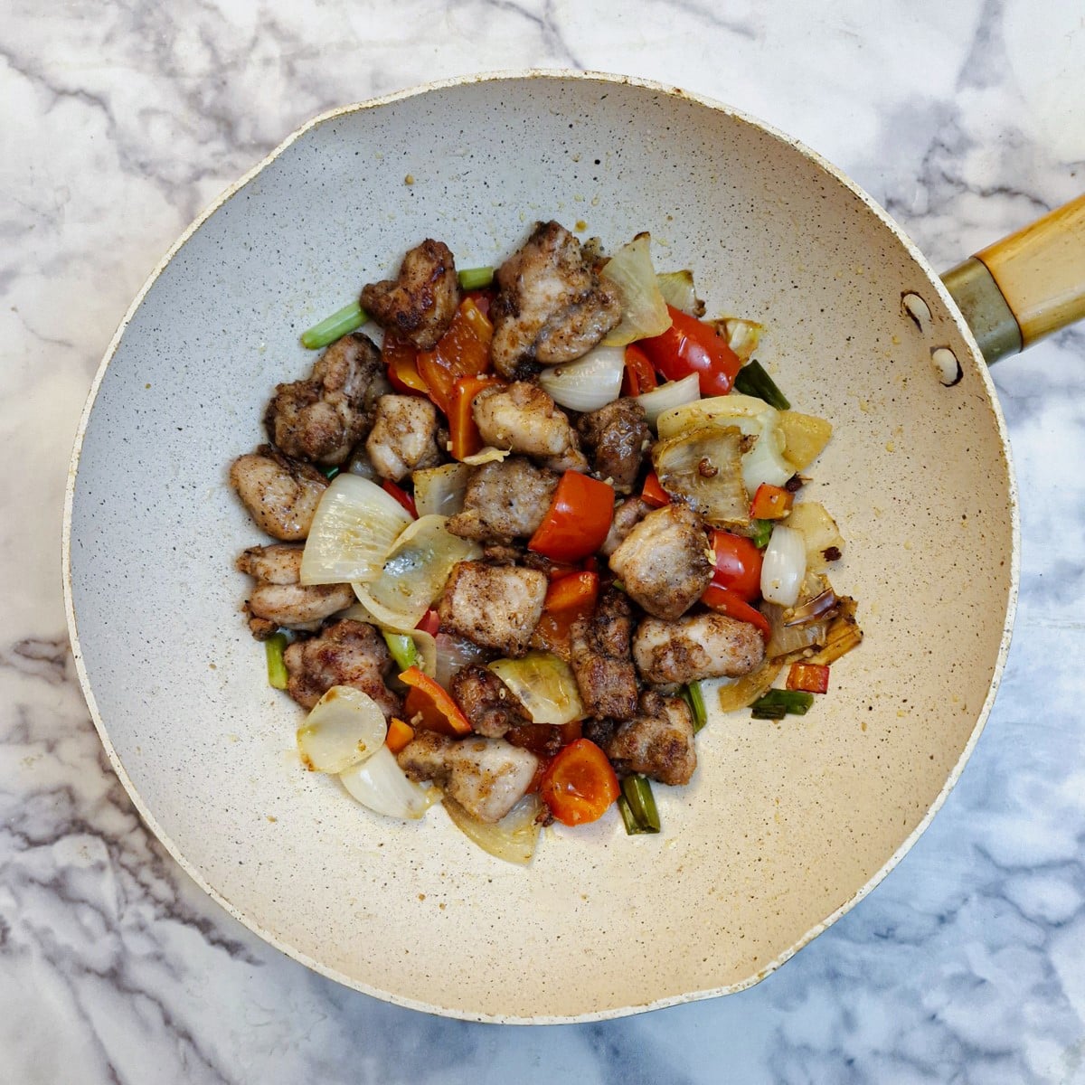 Fried chicken pieces mixed with onions and red peppers in a wok.