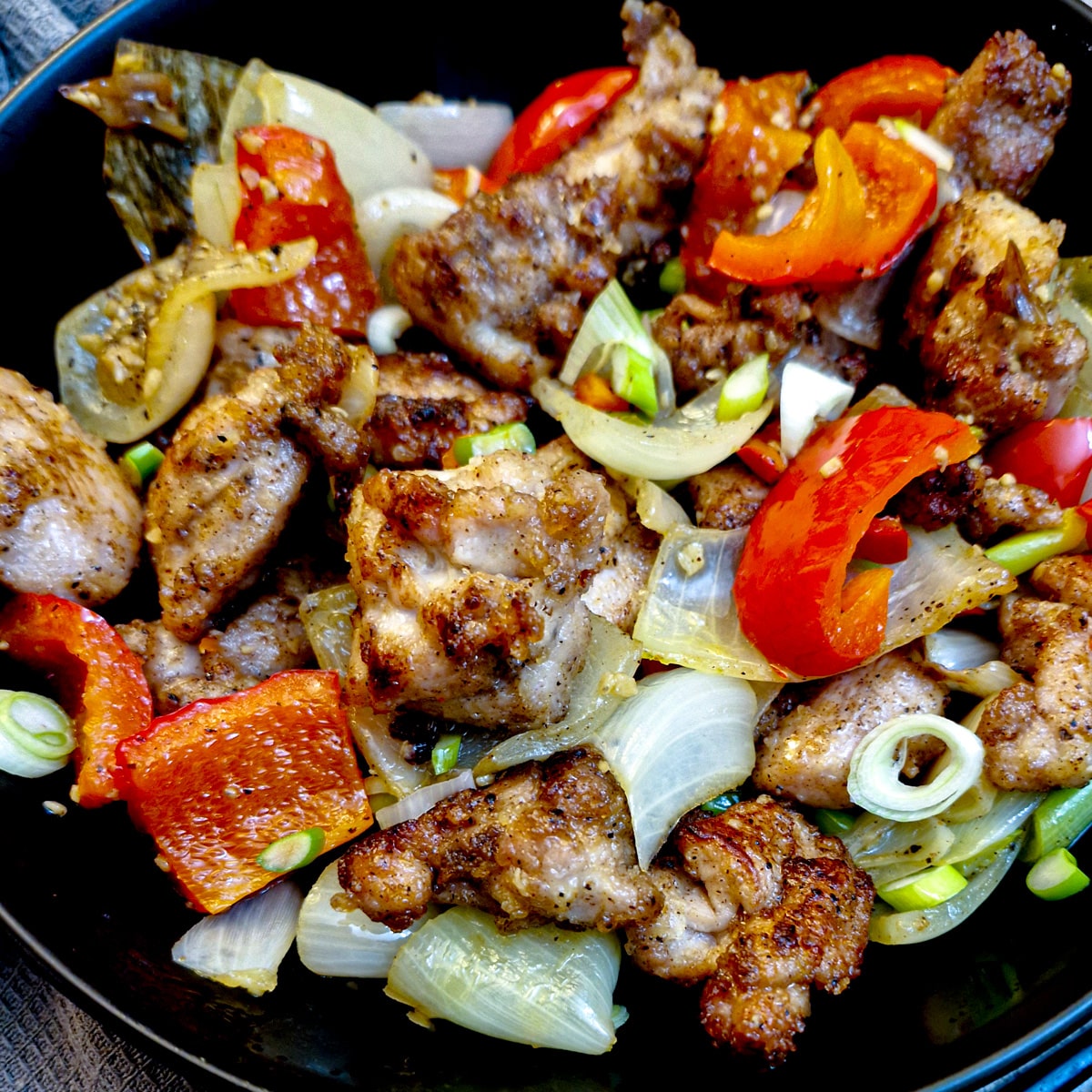 Close up of a dish of salt and pepper chicken garnished with extra chopped spring onions.