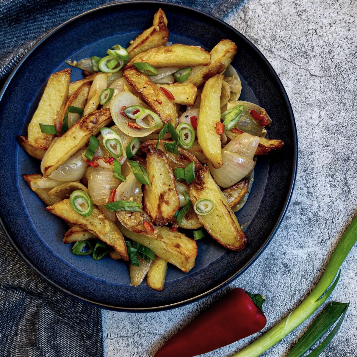 A blue serving dish of salt and pepper chips garnished with spring onions.