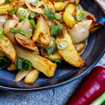 A plate of salt and pepper chips in a blue serving bowl next to a red chilli