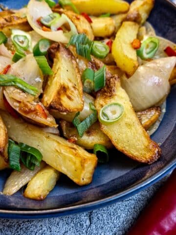 A plate of salt and pepper chips in a blue serving bowl next to a red chilli