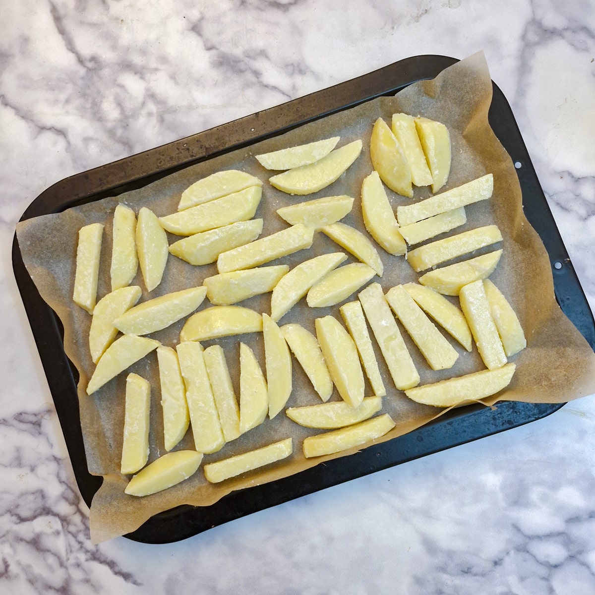 A baking tray lined with baking parchment with a single layer of chips arranged on it.