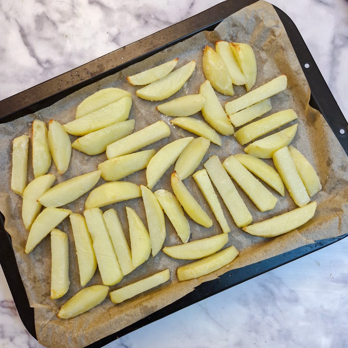 Half-cooked chips on a baking tray.