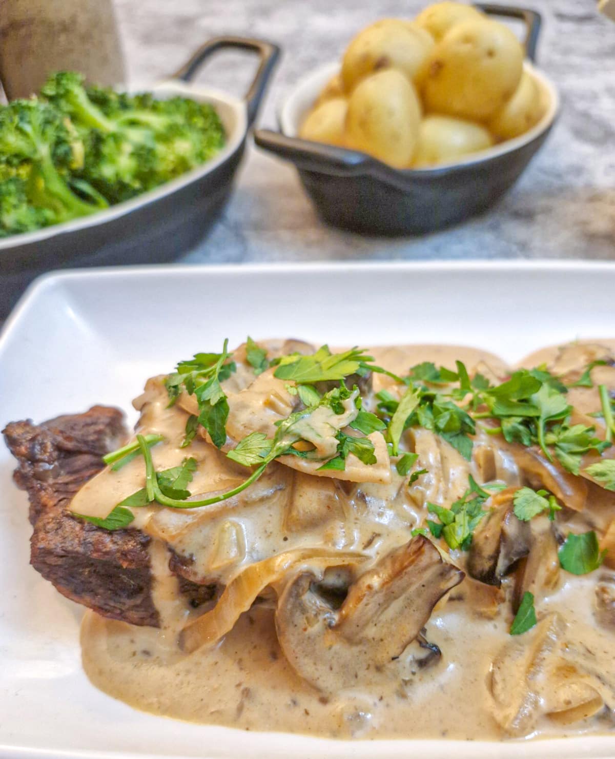 Close up of a piece of flat iron steak on a plate, covered with mushroom and onion sauce.