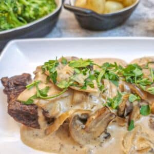 Close up of a piece of flat iron steak on a plate, covered with mushroom and onion sauce.