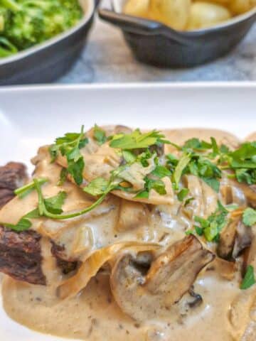 Close up of a piece of flat iron steak on a plate, covered with mushroom and onion sauce.