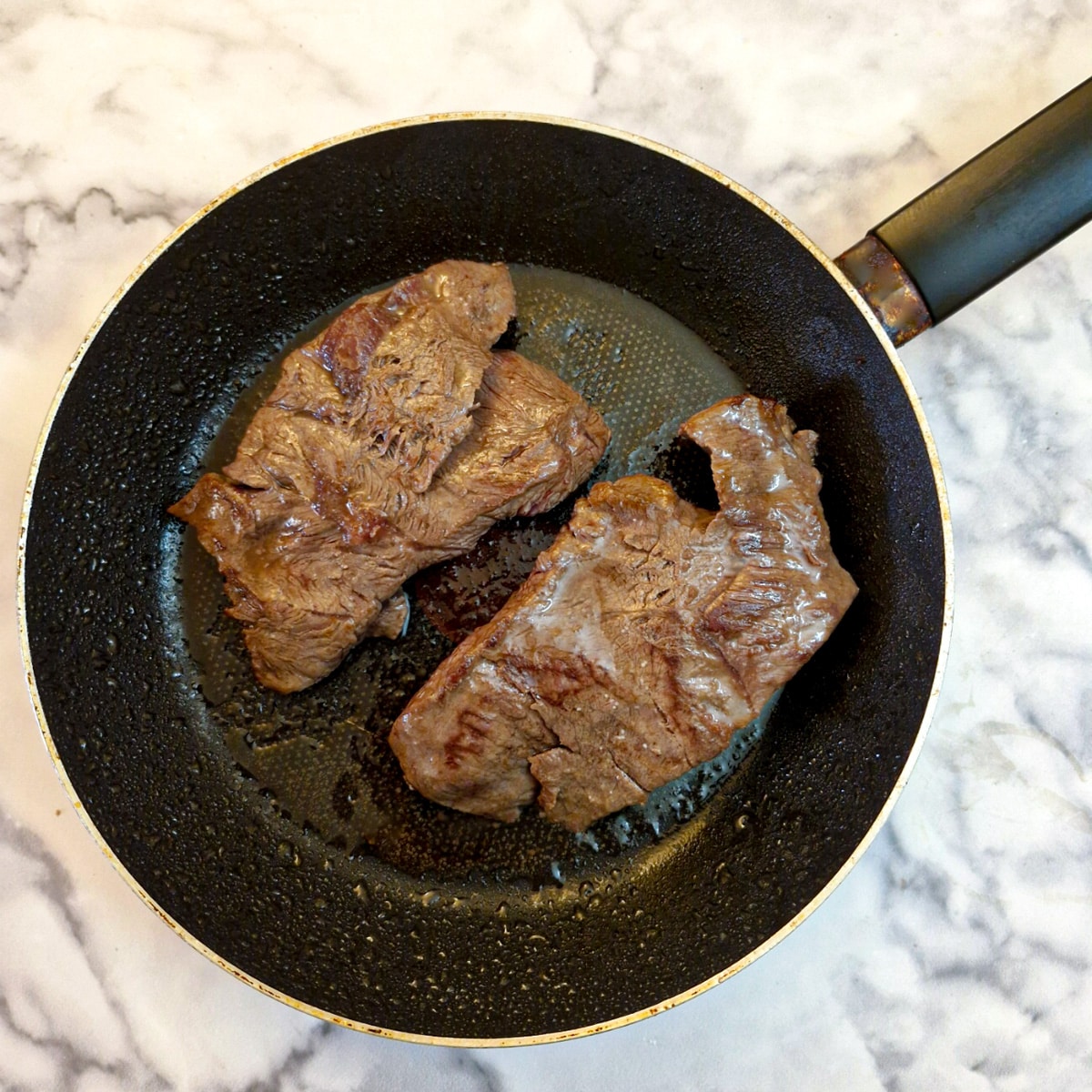 2 pieces of flat iron steak being seared in a frying pan.