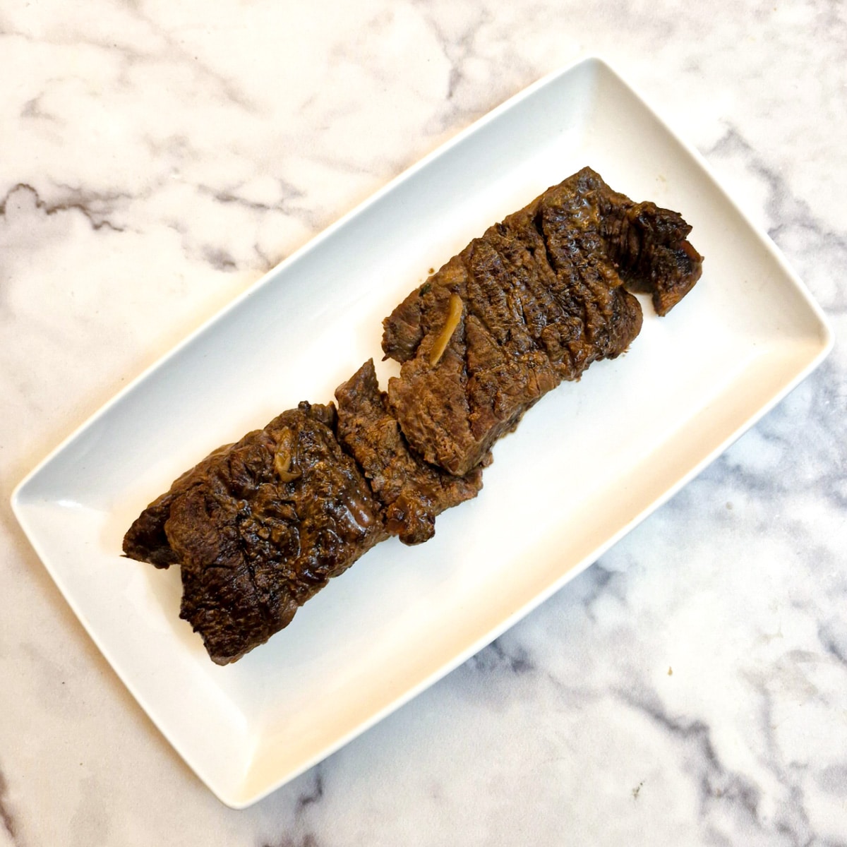 Cooked flat iron steak on a white oblong serving plate.