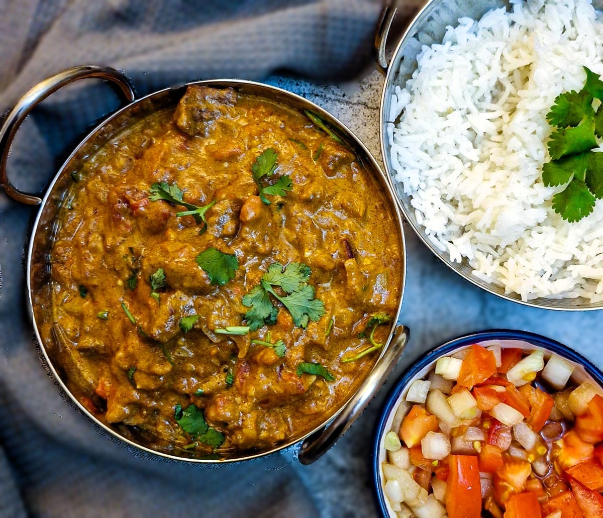 Overhead shot of a dish of beef madras curry, boiled rice and tomato sambal.