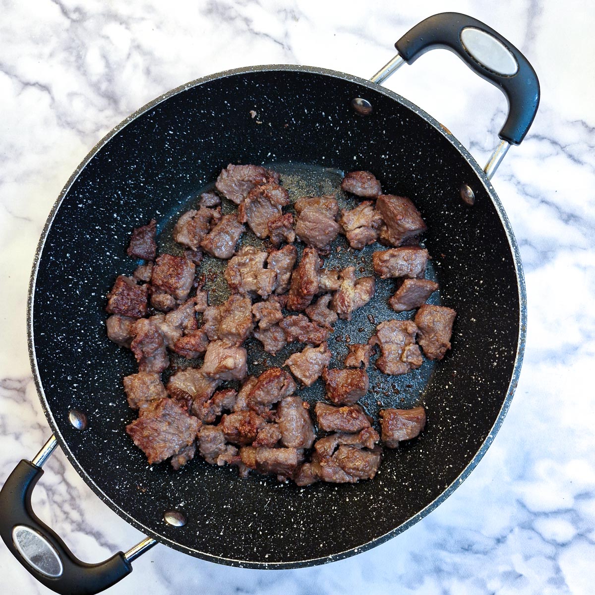 Pieces of flour-coated beef browning in a large frying pan.