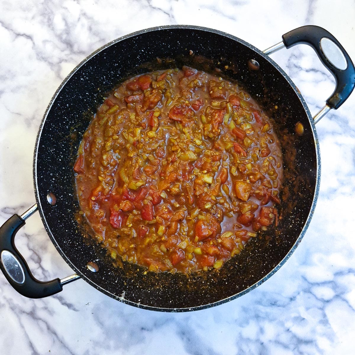 Tinned tomatoes added to onions and spices in a frying pan.