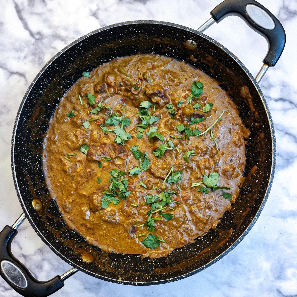 Beef madras curry garnished with coriander leaves in a frhying pan.