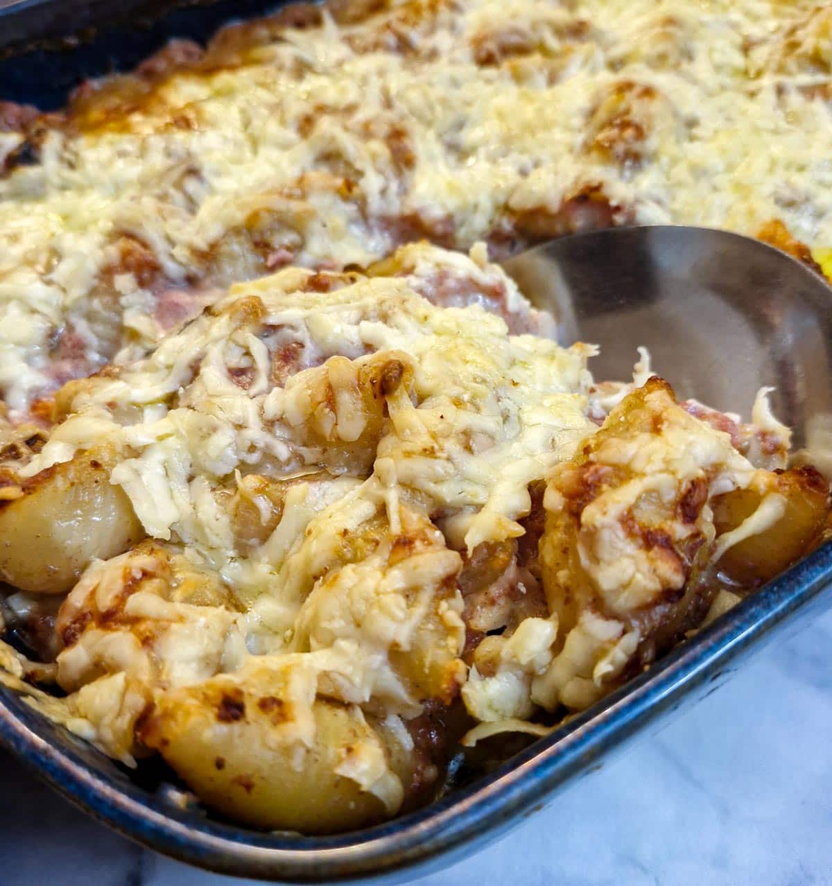 Bully beef pasta being spooned from a baking dish.