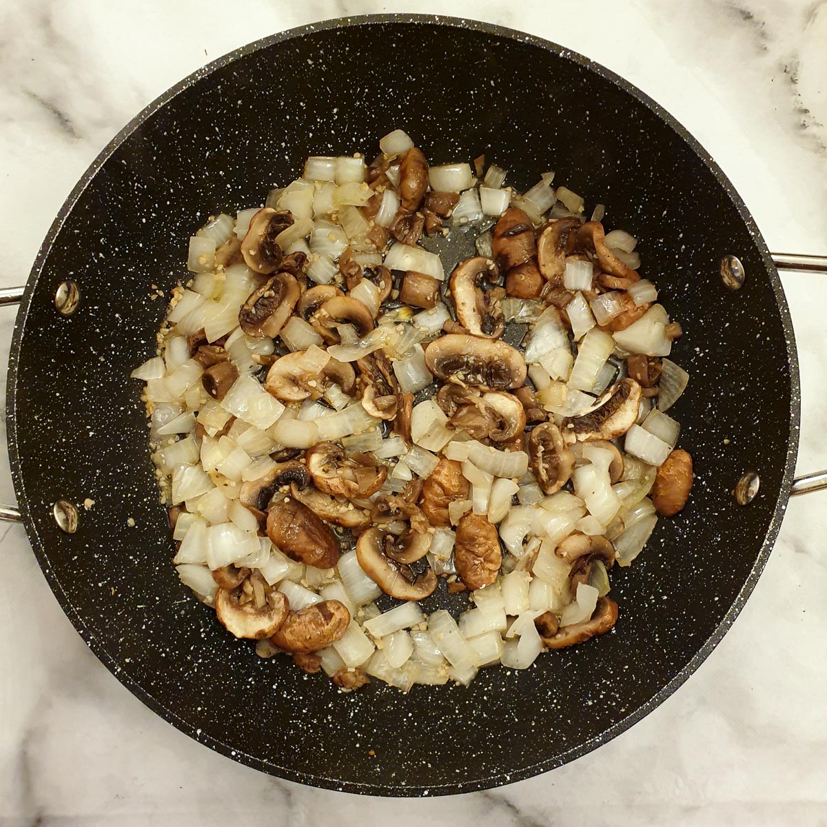 Chopped mushrooms and onions in a frying pan.