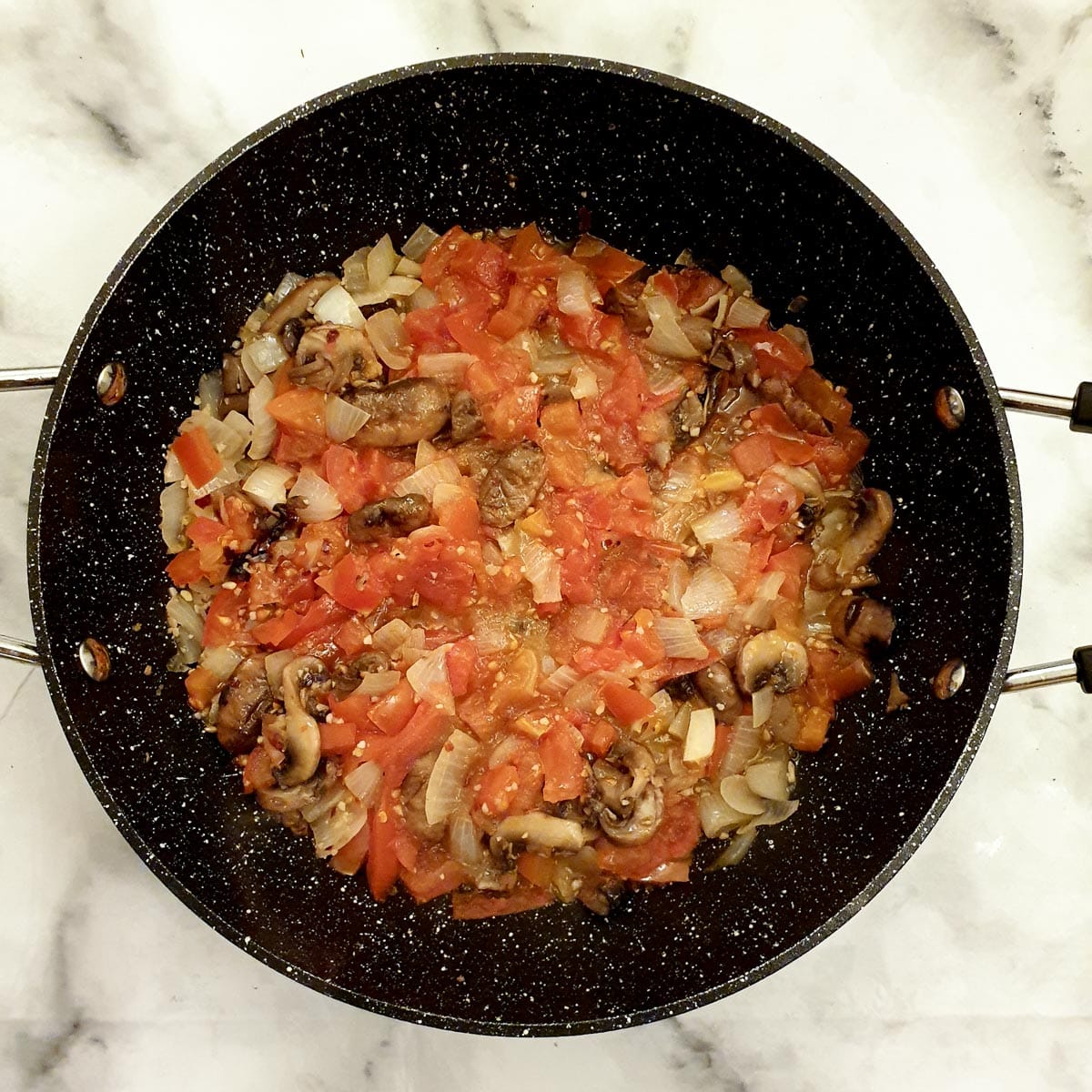 Tomatoes onions and mushrooms in a frying pan.