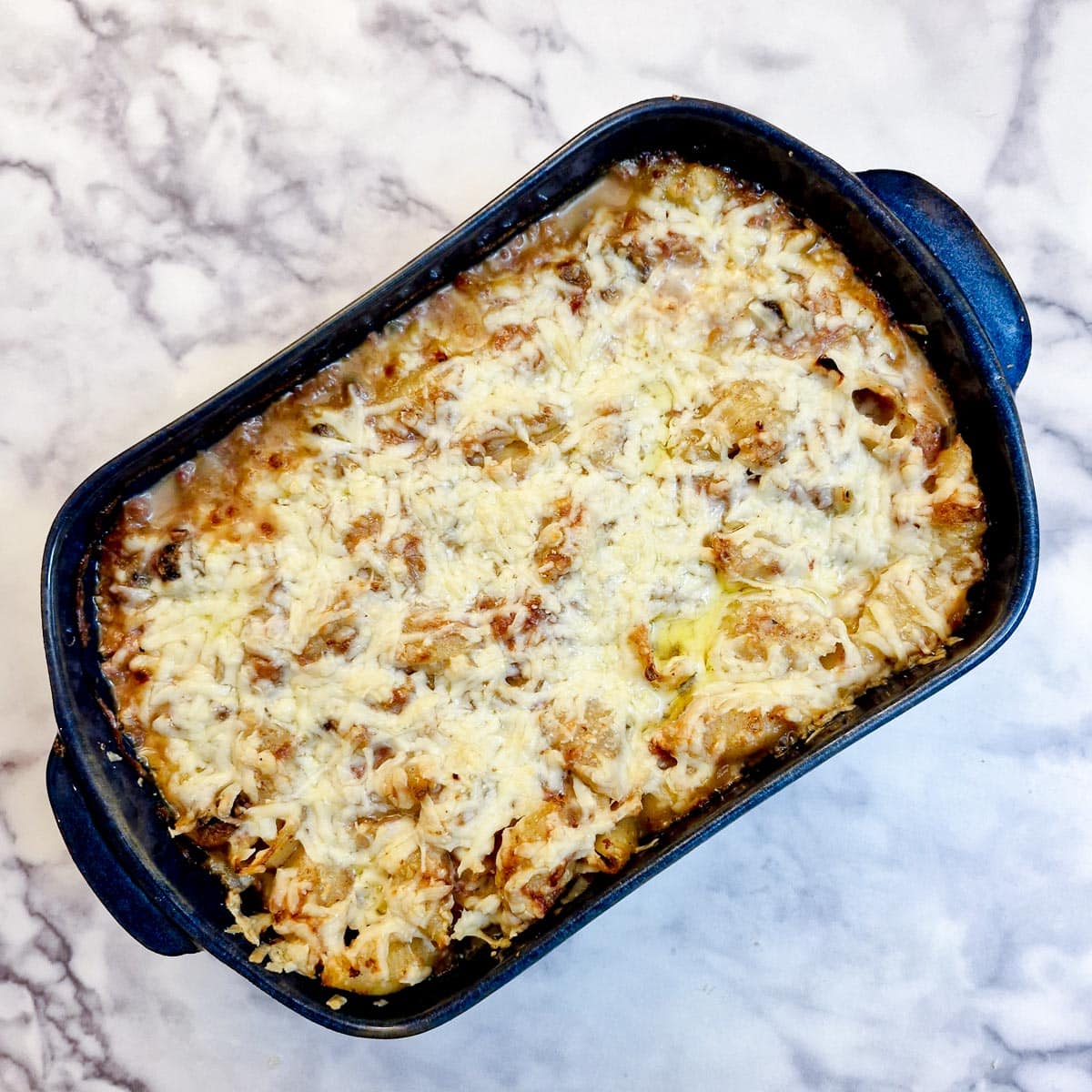 A dish of baked bully beef pasta covered with melted cheese.