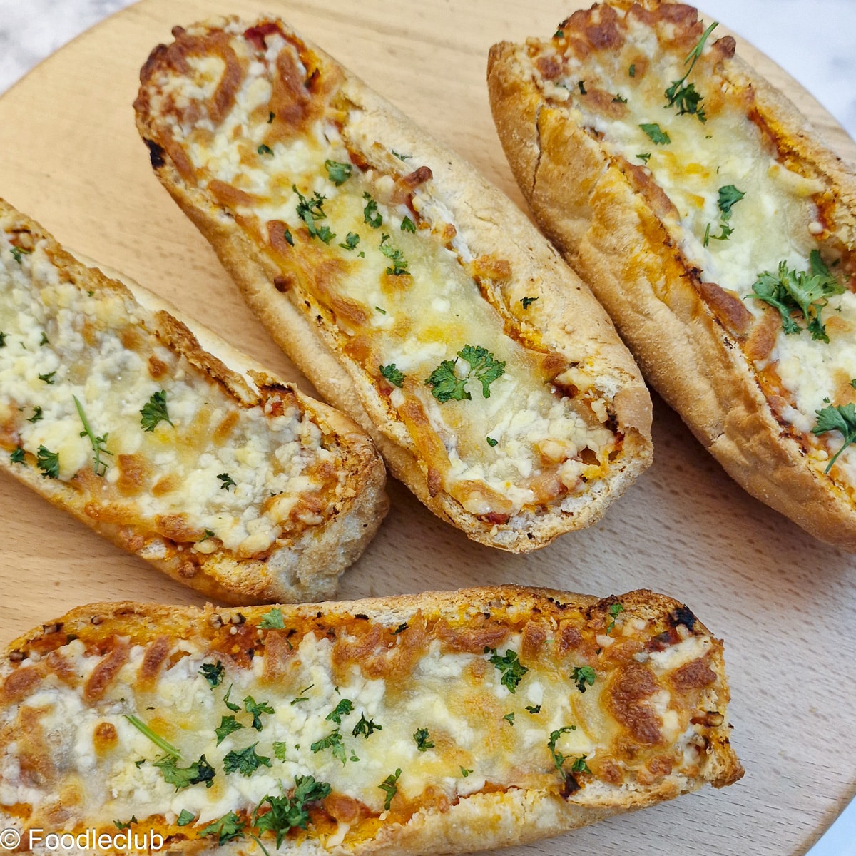 4 toasted cheesy garlic baguettes on a wooden platter.