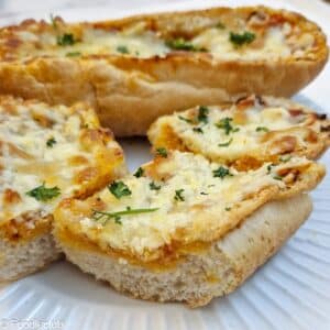 Side-on view of slices of cheese garlic baguette on a white plate.