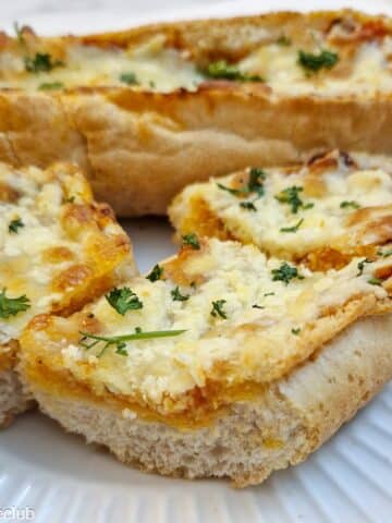 Side-on view of slices of cheese garlic baguette on a white plate.