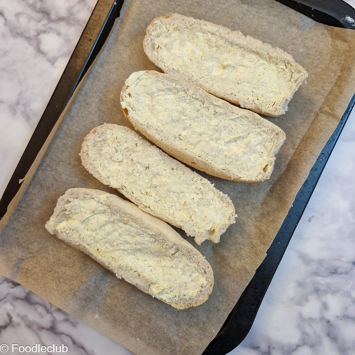 4 halved bread rolls spread with garlic butter on a baking tray.