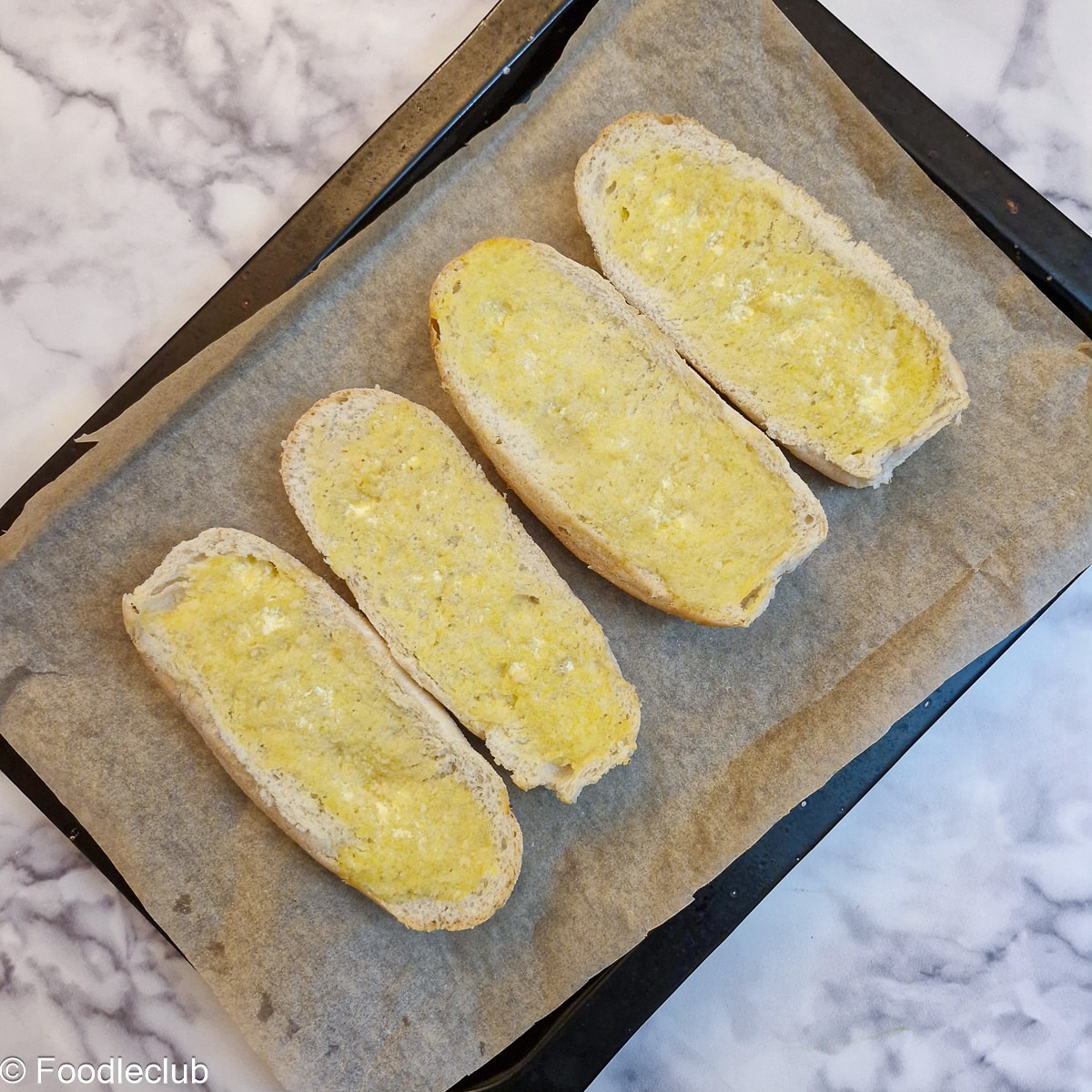 4 halved bread rolls spread with garlic butter on a baking tray after being toasted.