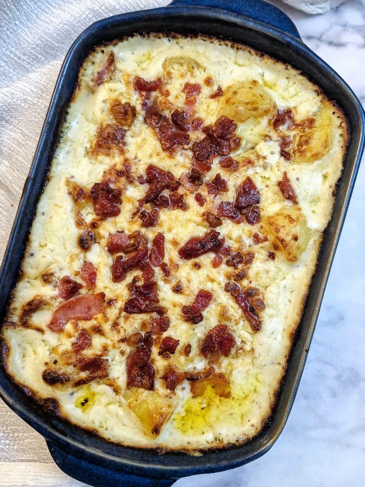 Overhead shot of a dish of cheesy potato casserole topped with grated cheese and bacon pieces.