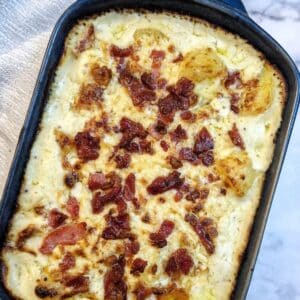 Overhead shot of a dish of cheesy potato casserole topped with grated cheese and bacon pieces.