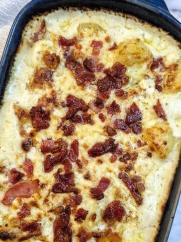 Overhead shot of a dish of cheesy potato casserole topped with grated cheese and bacon pieces.