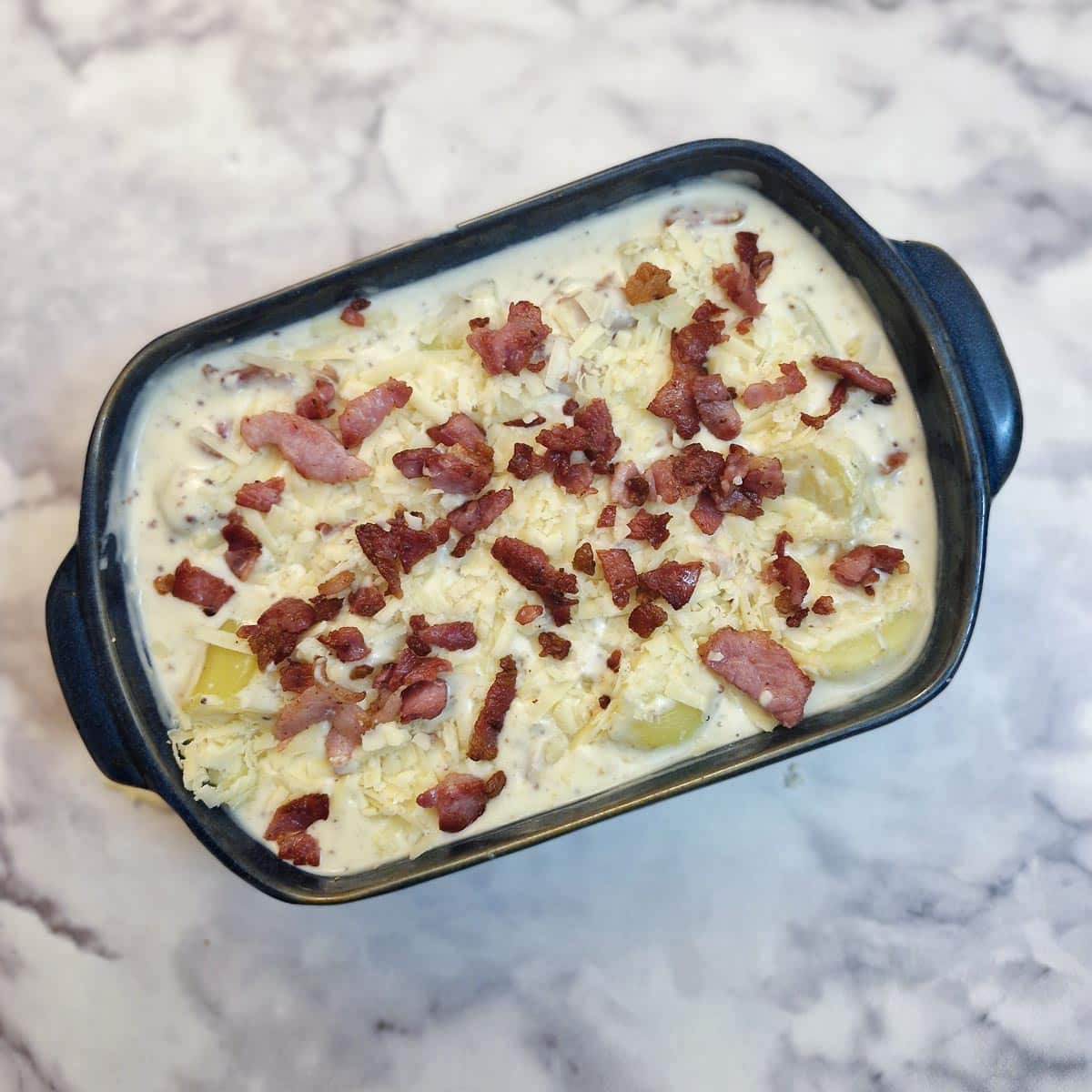 A cheesy potato casserole covered with grated cheese and bacon ready to go into the oven.