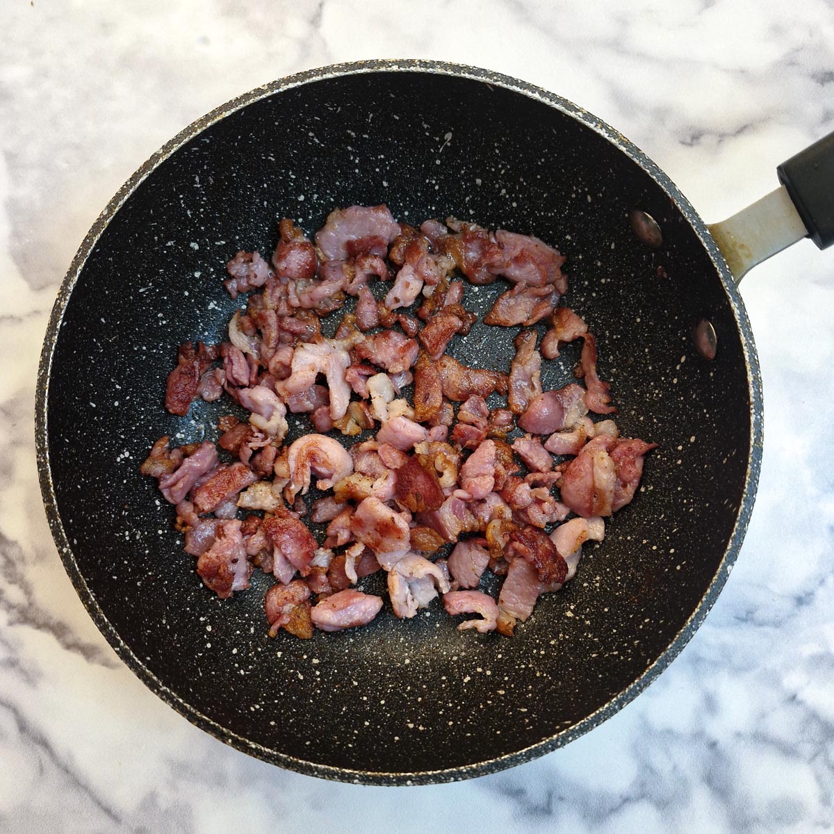 Pieces of bacon frying in a frying pan.