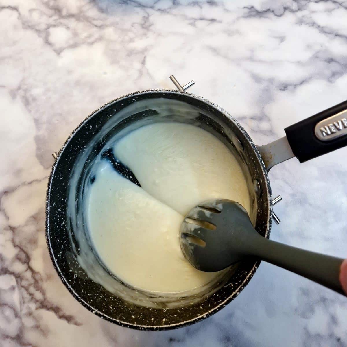 White sauce in a saucepan showing how a spoon leaves a trail when drawn through the sauce.