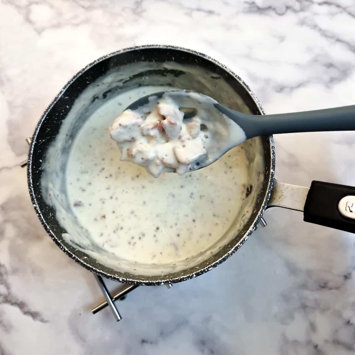 Pieces of bacon on a spoon being mixed into the cheese sauce.