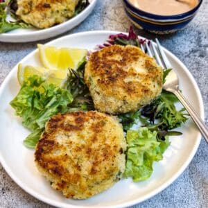 Two salmon fishcakes on a white plate on a bed of lettuce with lemon slices.