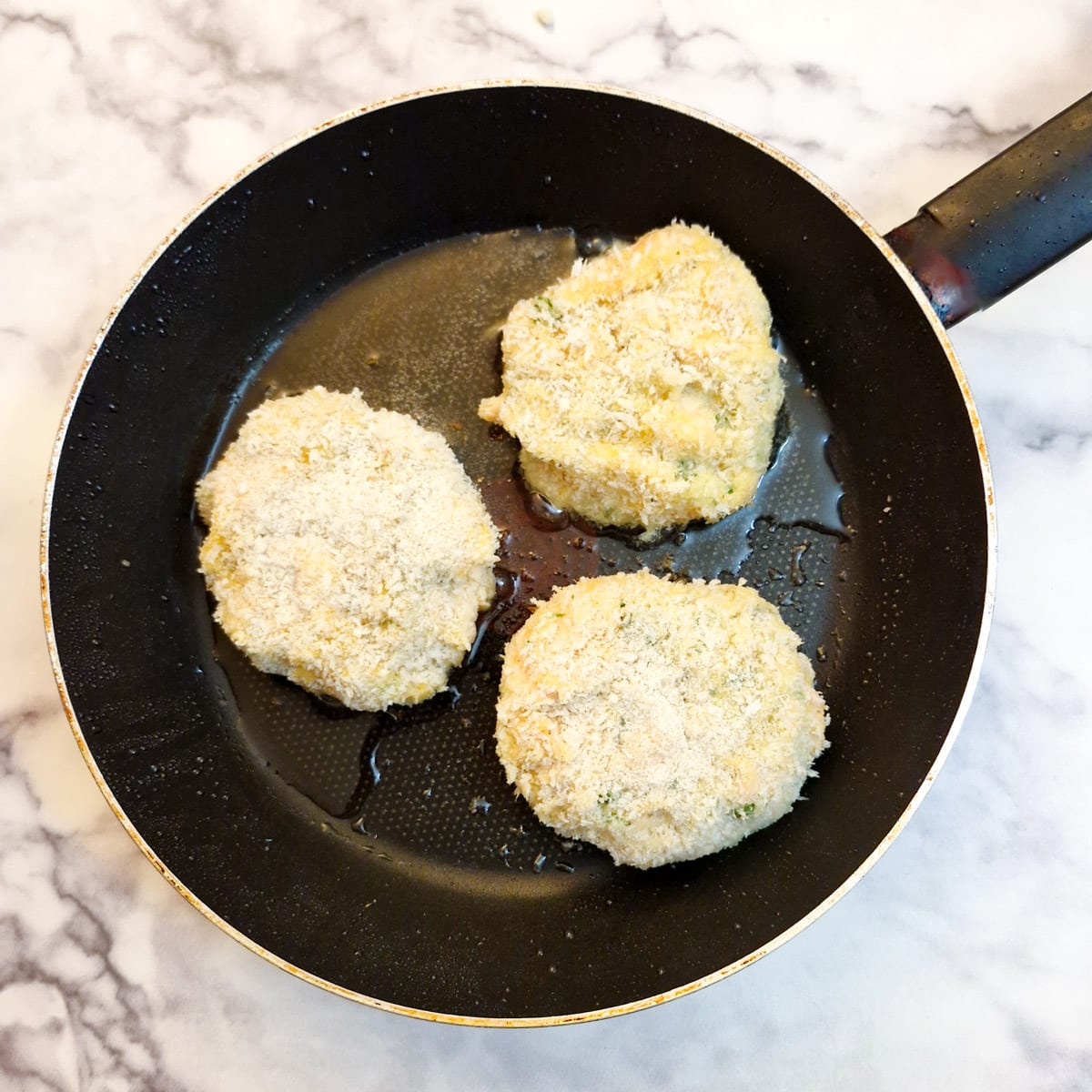 3 salmon fishcakes in a frying pan.