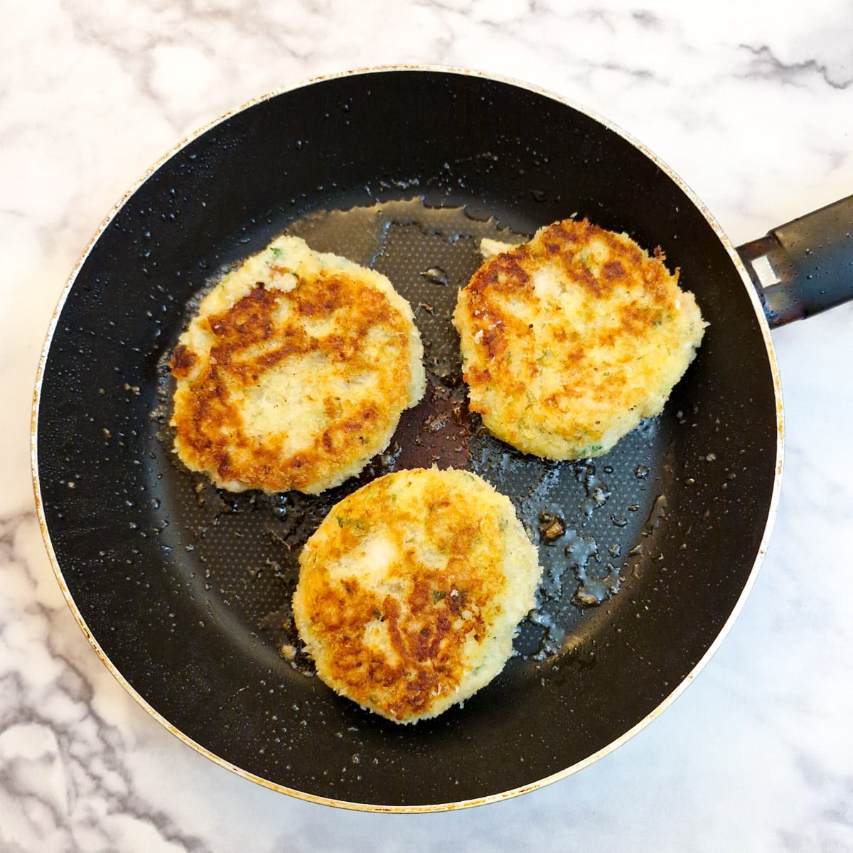 3 browned salmon fishcakes in a frying pan.