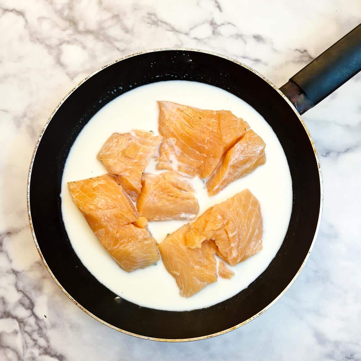 Salmon filets in a frying pan of milk.