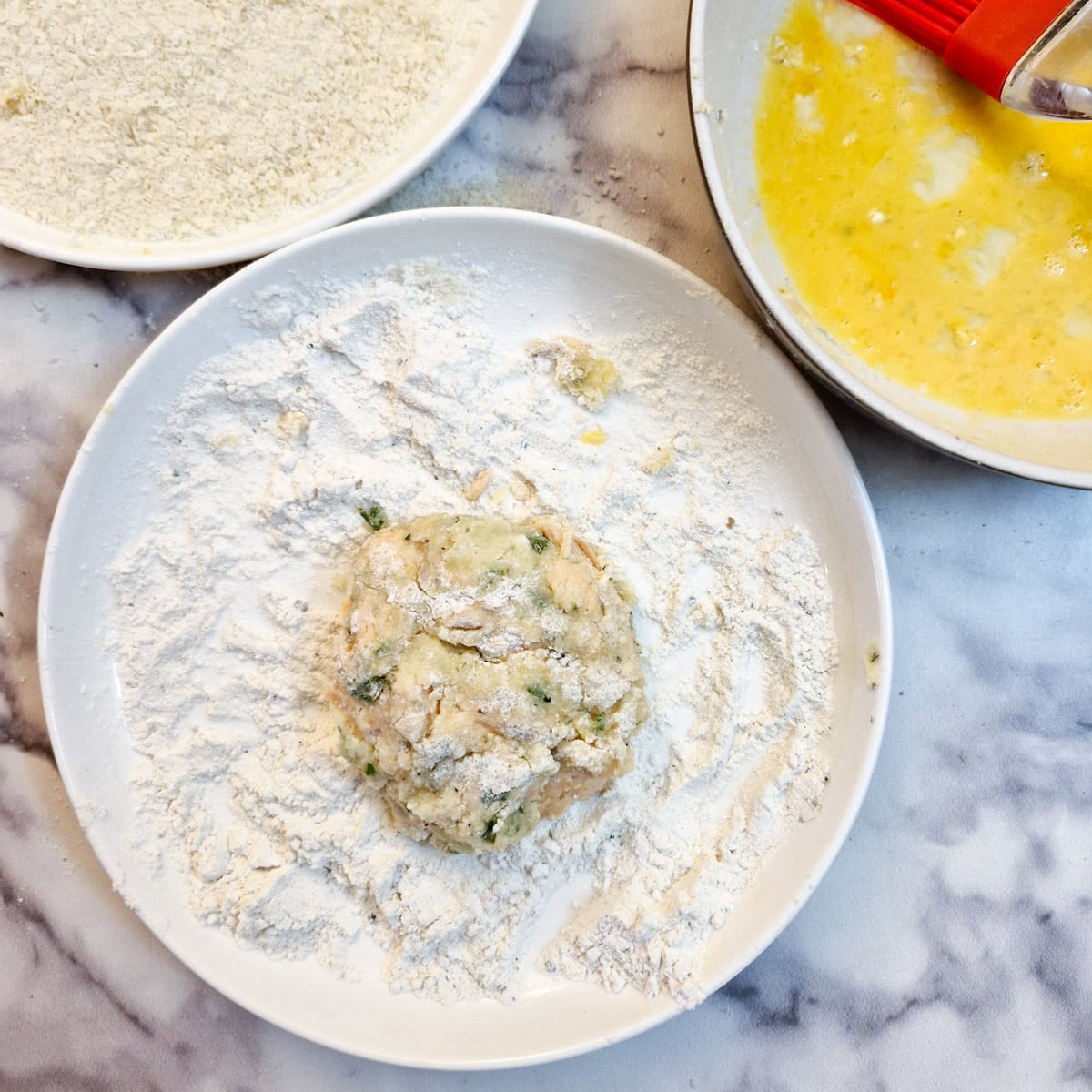 A fish patty in a bowl of flour.