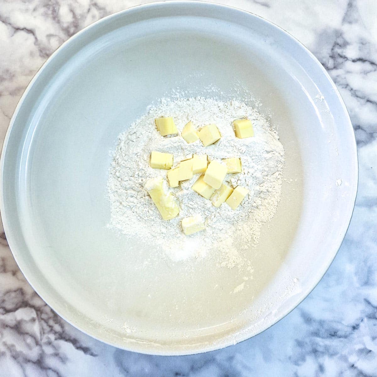 Flour and cubed butter in a large white mixing bowl.