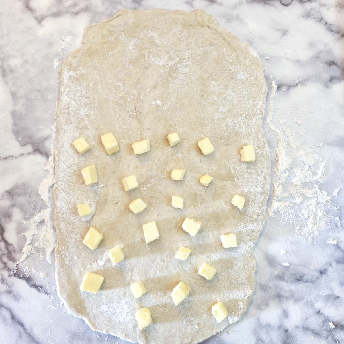 Pieces of butter dotted onto the bottom two thirds of a pastry rectangle.