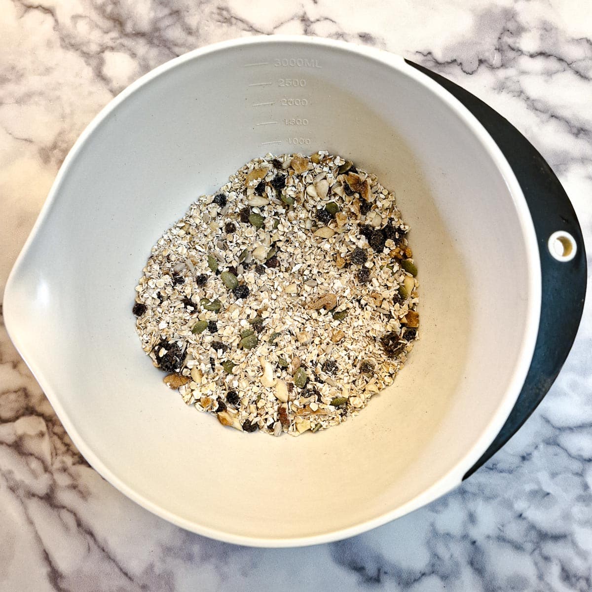 Dry ingredients for fruit and nut bars mixed together in a white mixing bowl.