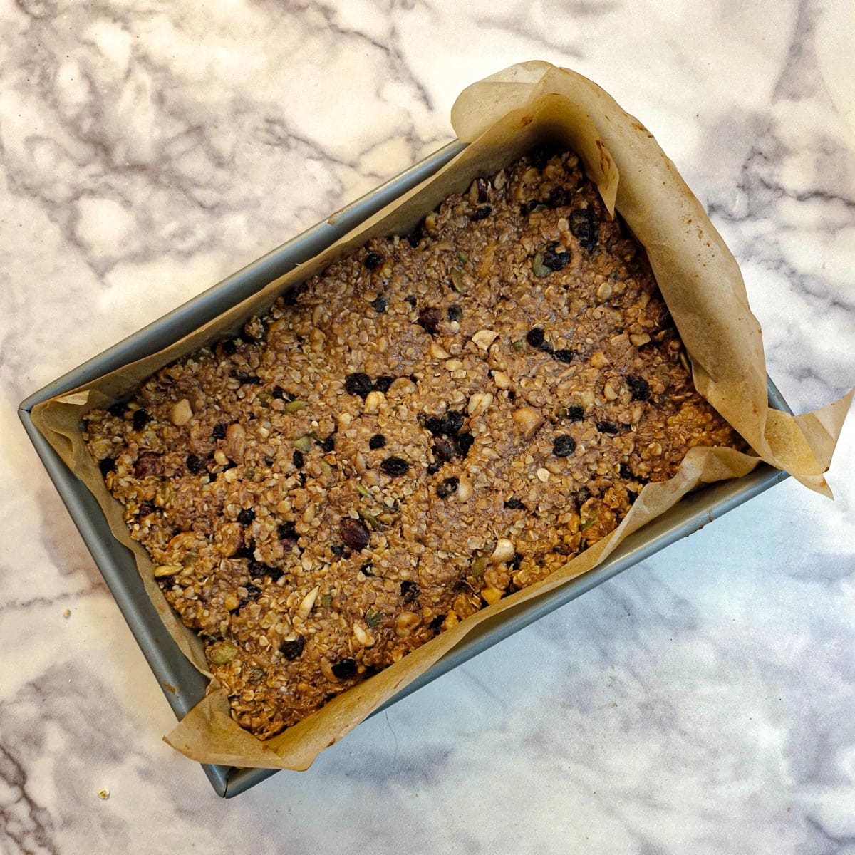 Fruit and nut muesli mixture pressed into a baking dish lined with baking parchment.